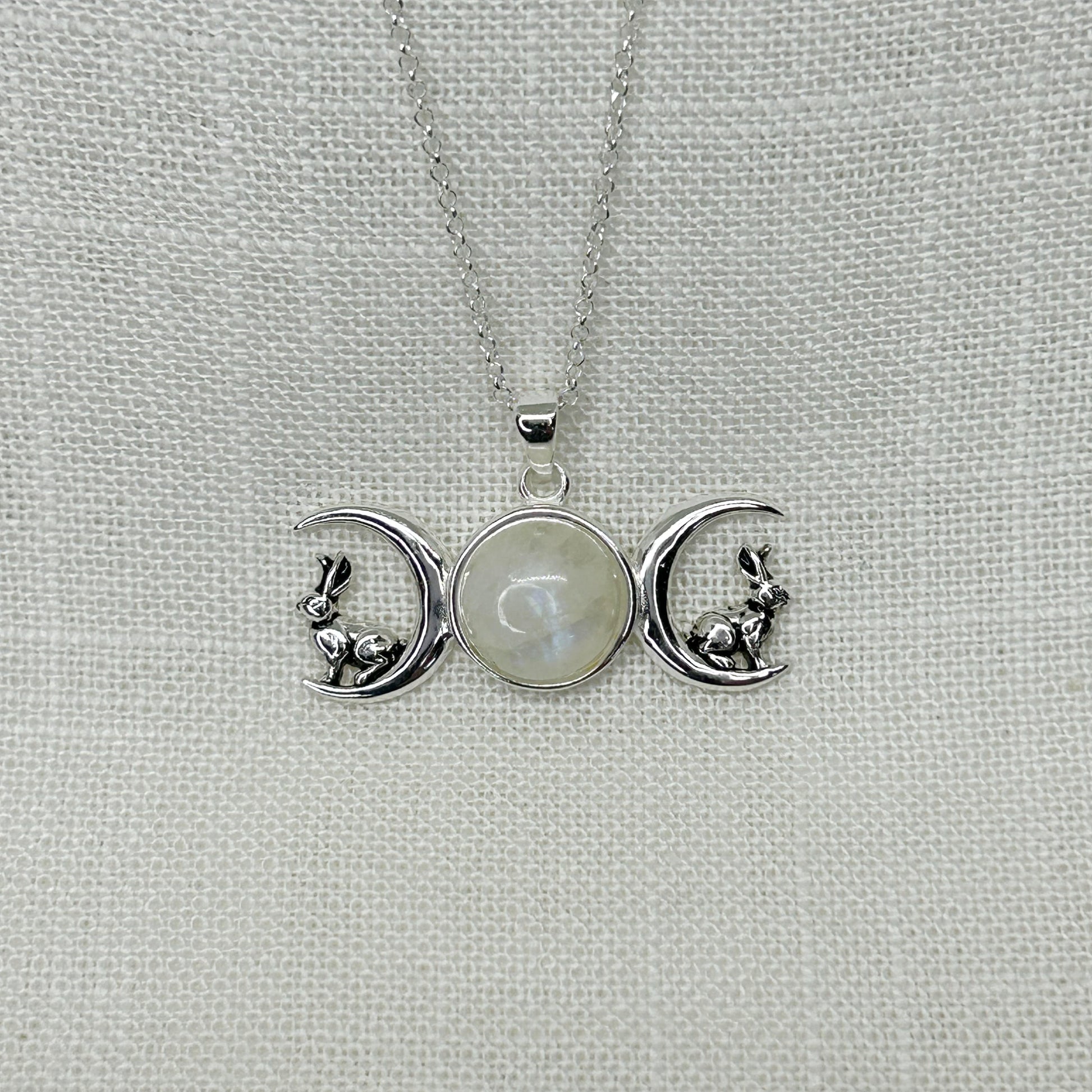 This 925 silver triple moon hare necklace is approx 3.5cm long by 2cm high including its bale. Featuring a 1.1cm diameter by 7mm depth rainbow moonstone cabochon in the centre as the full moon, together with a waxing and waning moon on either side.